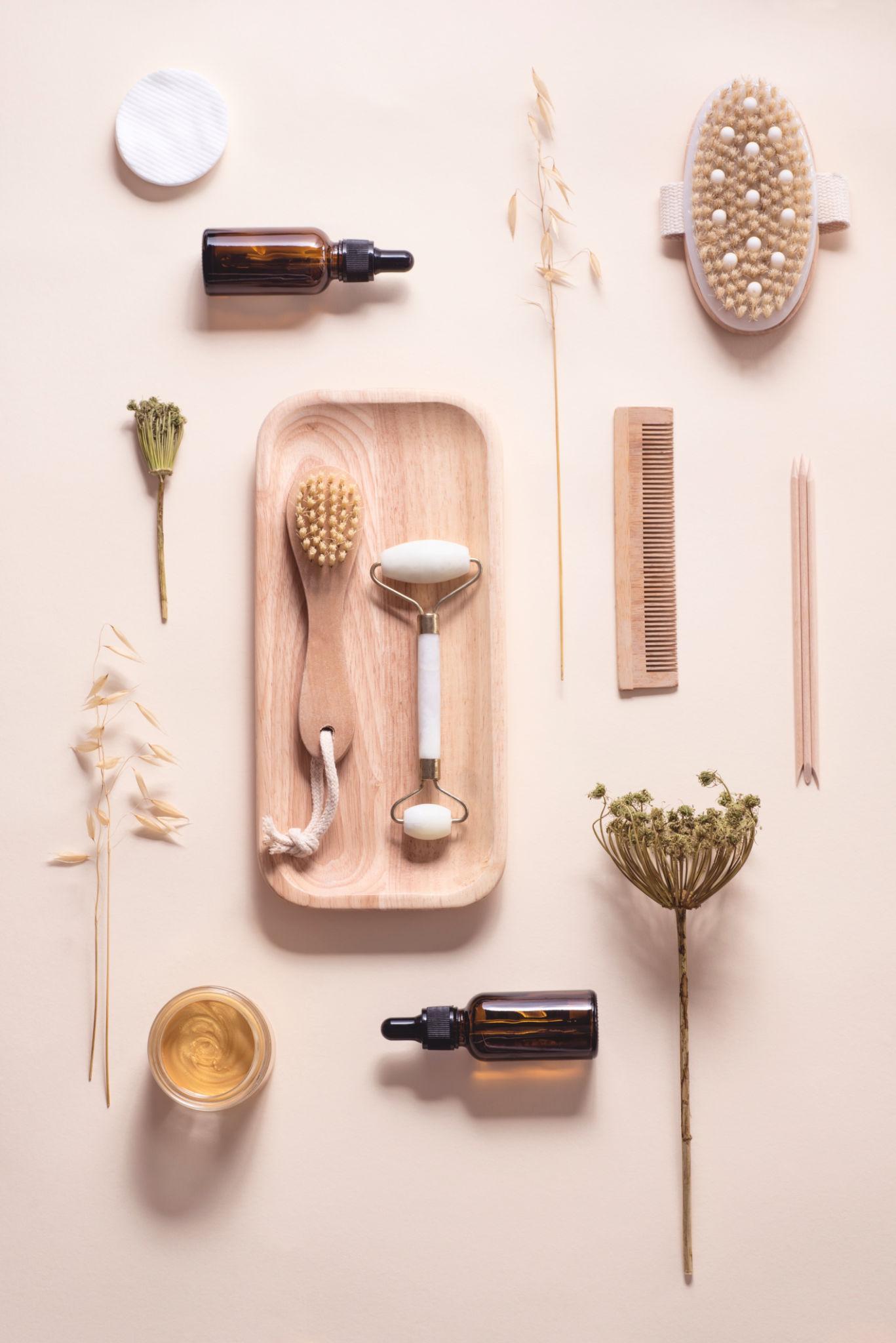Jade roller, botanical dropper serums and dried florals arranged on warm beige linen